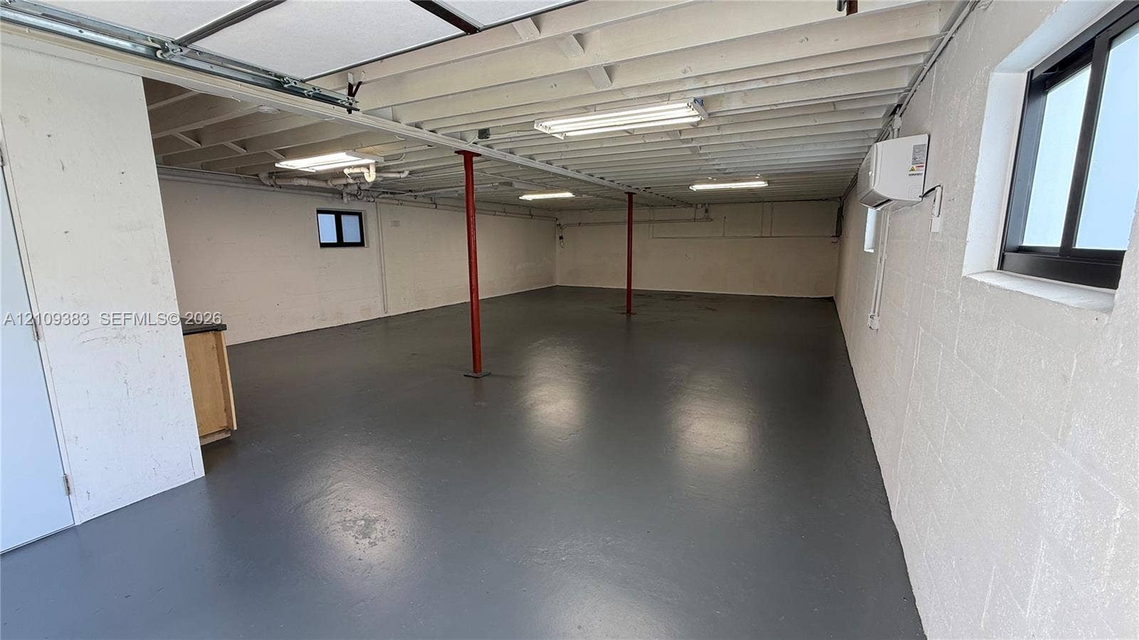 10751 SW 48th Street, Davie, Davie, FL 33328 Open interior featuring painted concrete block walls, finished floor surfacing, exposed ceiling joists, overhead fluorescent lighting, and wall-mounted HVAC unit
