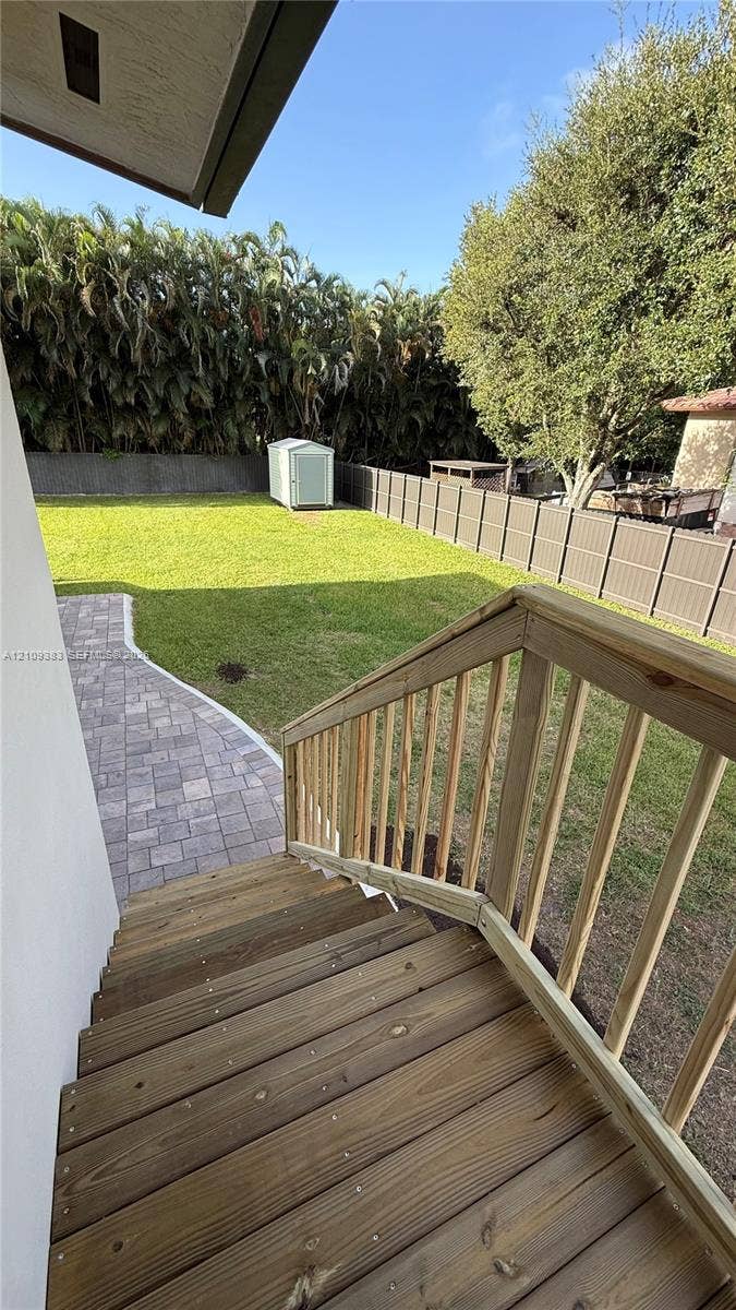 10751 SW 48th Street, Davie, Davie, FL 33328 Backyard featuring a wood-plank deck, stone-paver walkway, fenced perimeter, and dedicated storage shed