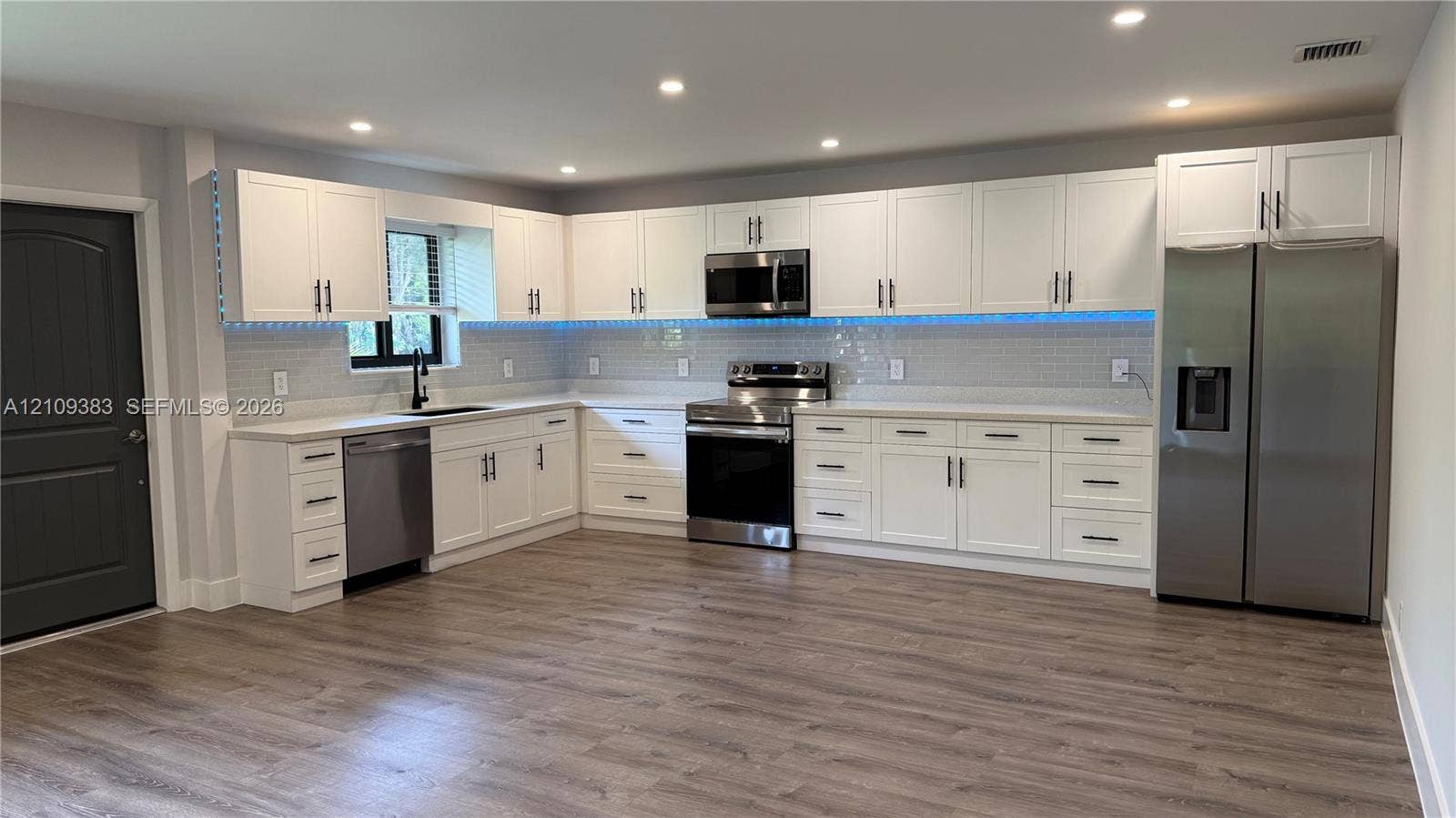 10751 SW 48th Street, Davie, Davie, FL 33328 Kitchen featuring white shaker-style cabinetry, stainless steel appliances, light-toned stone countertops, subway tile backsplash, and wood-finish flooring