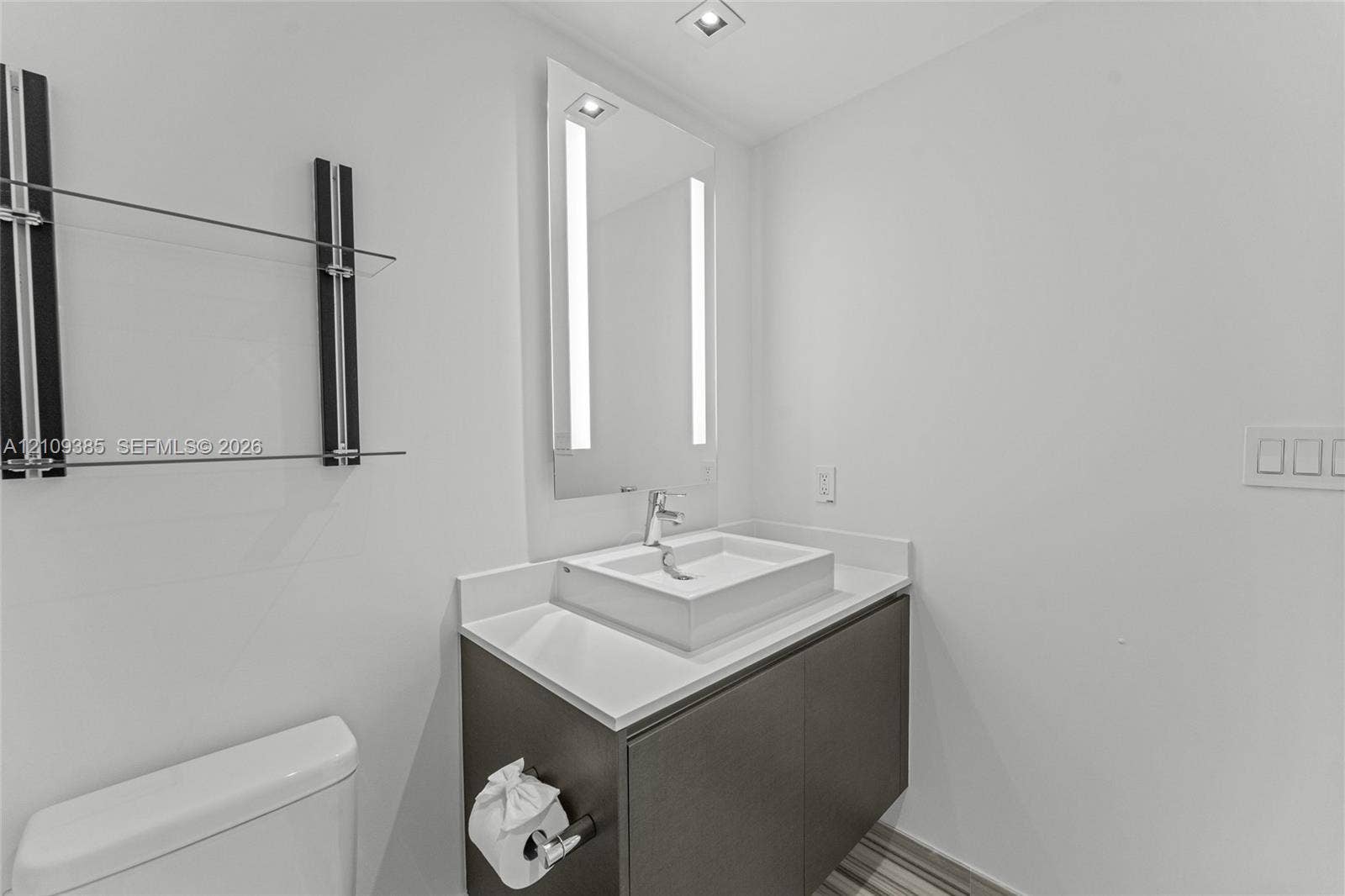 Floating vanity with a solid-surface countertop and rectangular vessel sink, integrated LED mirror, and wall-mounted glass shelving