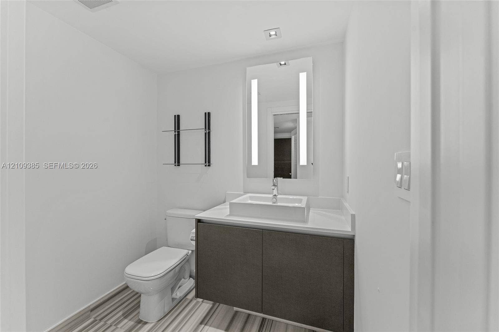 Wall-mounted vanity with a rectangular vessel sink and countertop, backlit rectangular mirror, and glass wall shelving