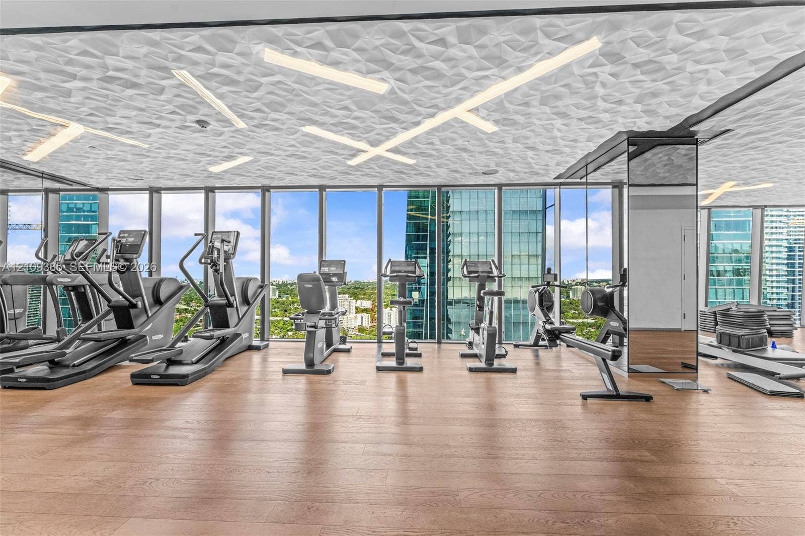 Fitness center featuring wood-finish flooring, floor-to-ceiling windows, and a geometric textured ceiling with integrated linear lighting