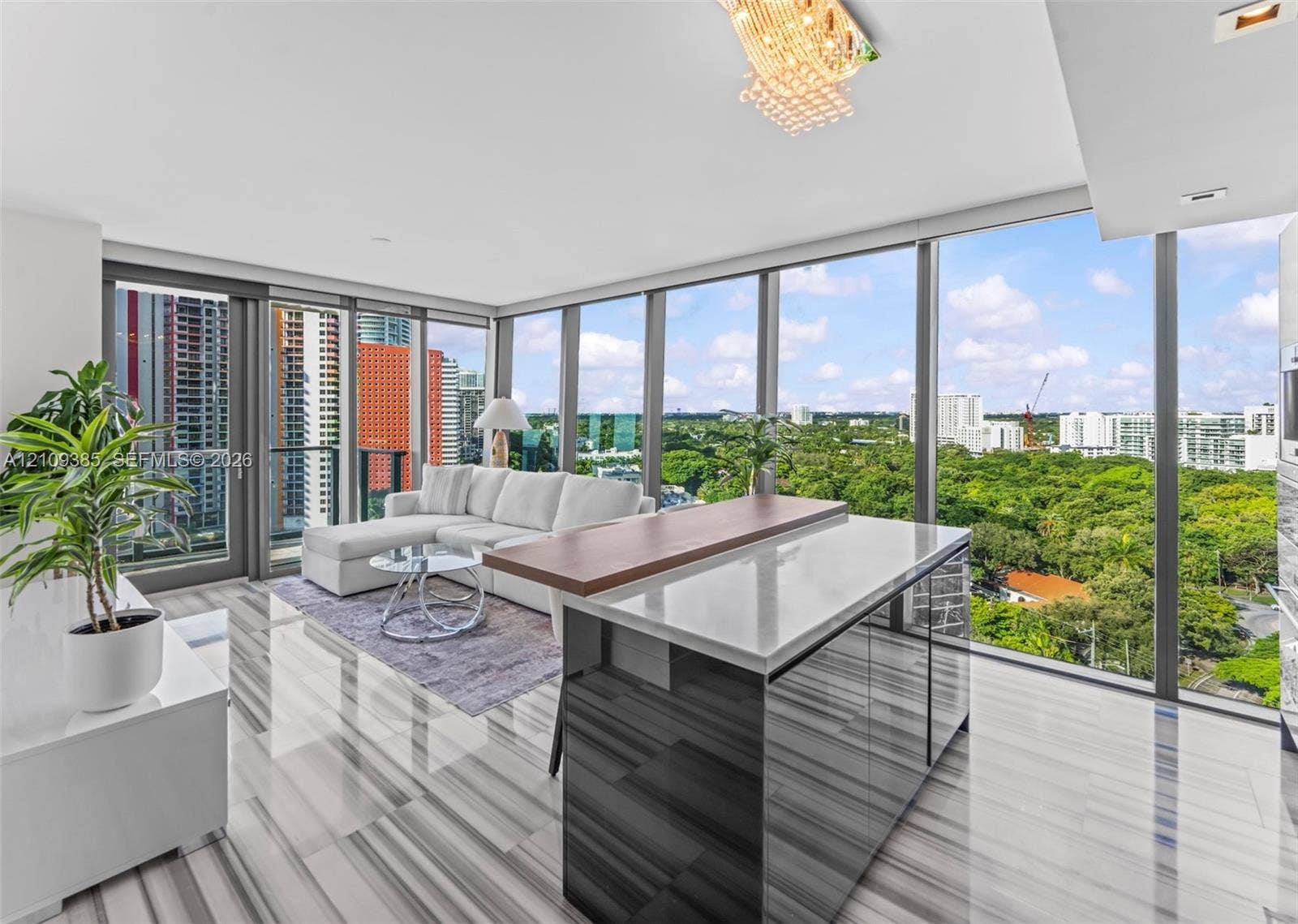 Floor-to-ceiling glass windows, kitchen island featuring a stone-finish countertop with a wood-finish breakfast bar, polished stone-finish flooring, and a decorative crystal chandelier