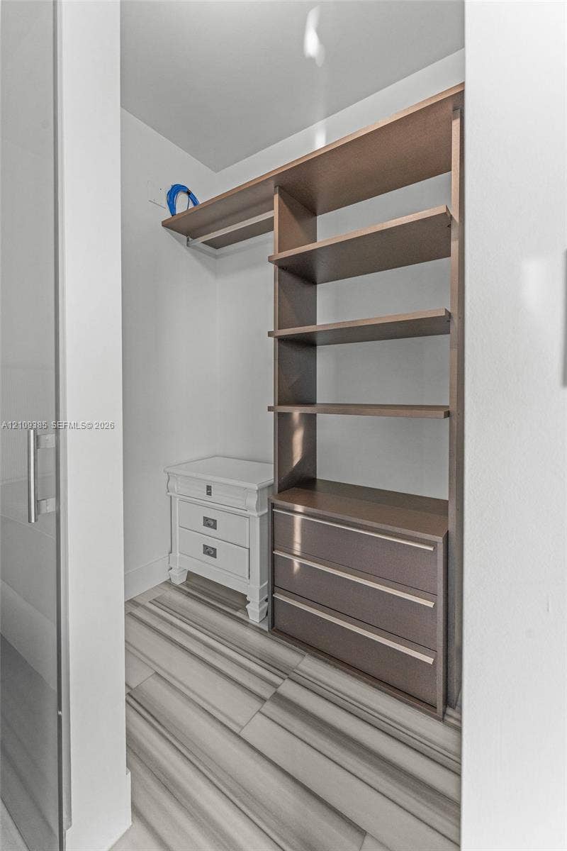 Walk-in storage space featuring wood-finish open shelving, built-in lower drawers, and tile flooring