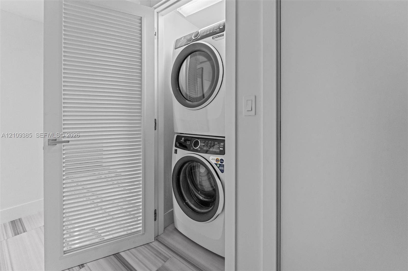 Laundry closet featuring a stacked front-load washer and dryer and a louvered door