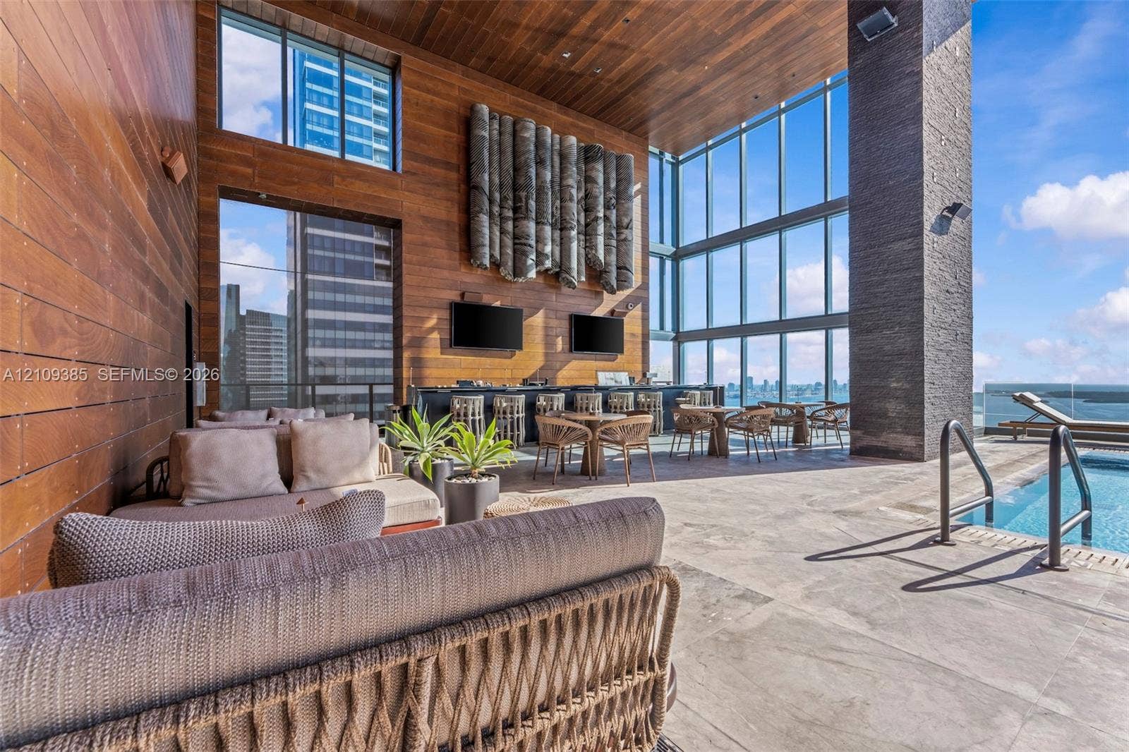 Outdoor lounge featuring wood-paneled walls and ceiling, floor-to-ceiling glass windows, stone-tiled flooring, and a recessed swimming pool with metal handrails