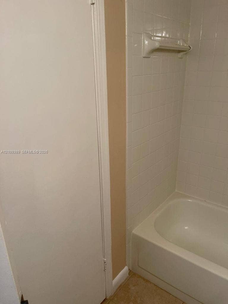 Bathtub featuring a white acrylic surround, wall-mounted white soap dish, and a built-in storage closet