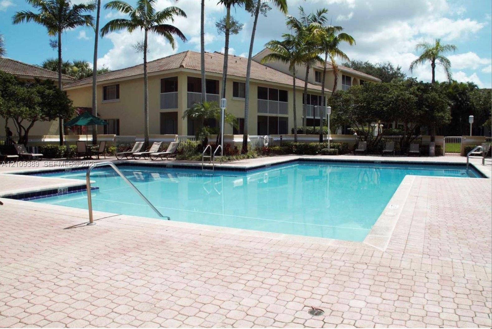 Swimming pool featuring a paved deck, metal handrails, and surrounding mature palm trees