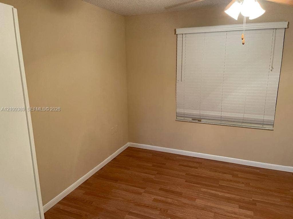 Wood-finish flooring, neutral wall tones, window with horizontal blinds, and a ceiling-mounted light fixture
