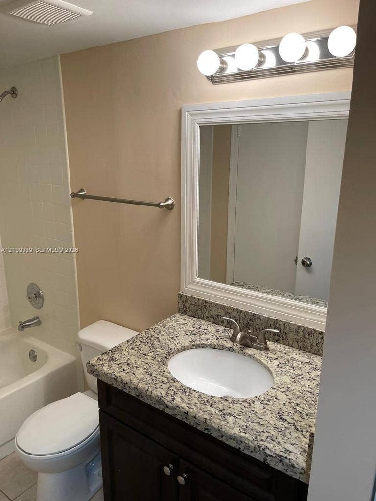 Vanity featuring a dark-finish wood cabinet, stone-look countertop, integrated oval sink, and chrome fixtures, paired with a framed wall mirror, multi-bulb vanity light, and a tiled shower-tub combination
