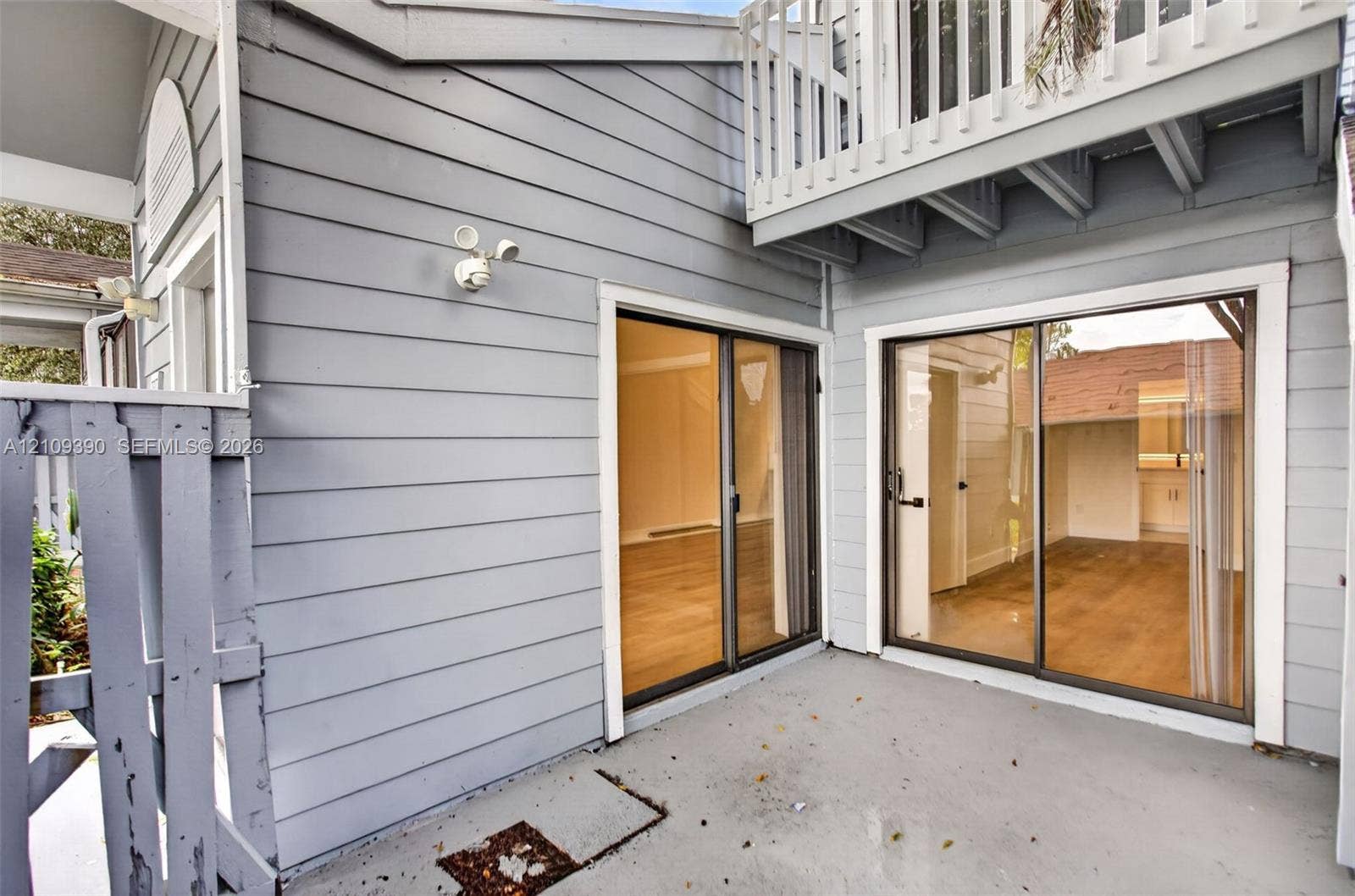 Exterior patio space featuring horizontal lap siding, two sets of glass sliding doors, and a wood-slat upper balcony