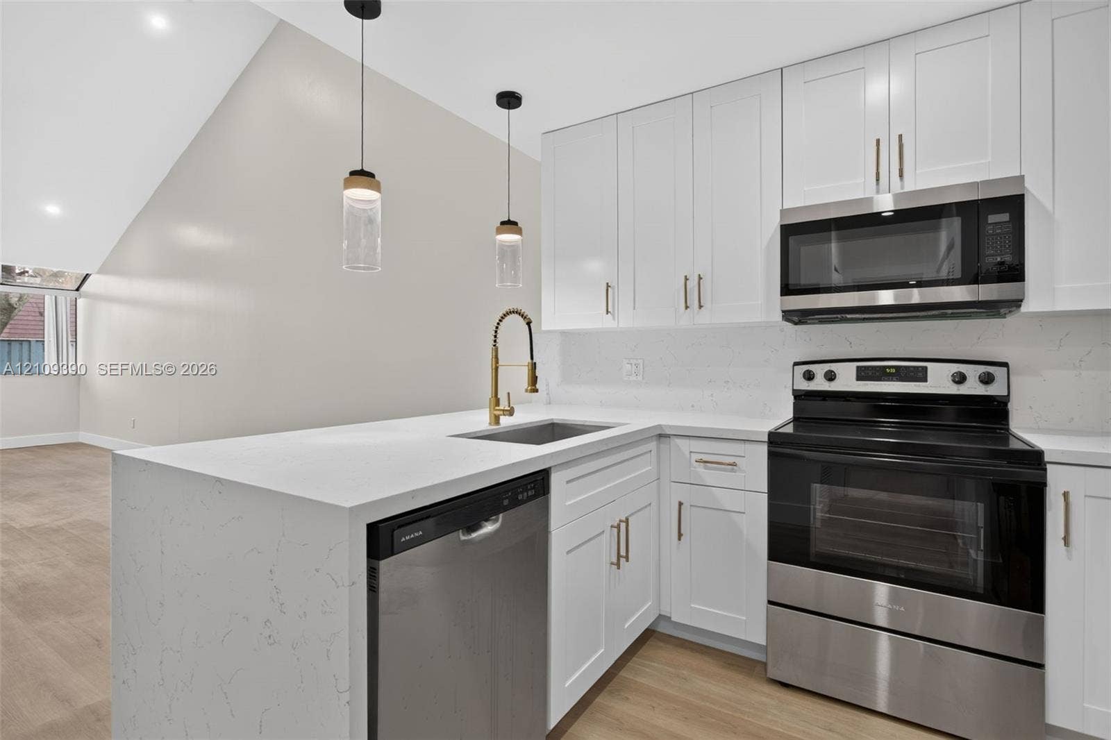 Kitchen featuring white shaker-style cabinetry, quartz countertops, stainless steel appliances, a brass-finish gooseneck faucet, and recessed pendant lighting