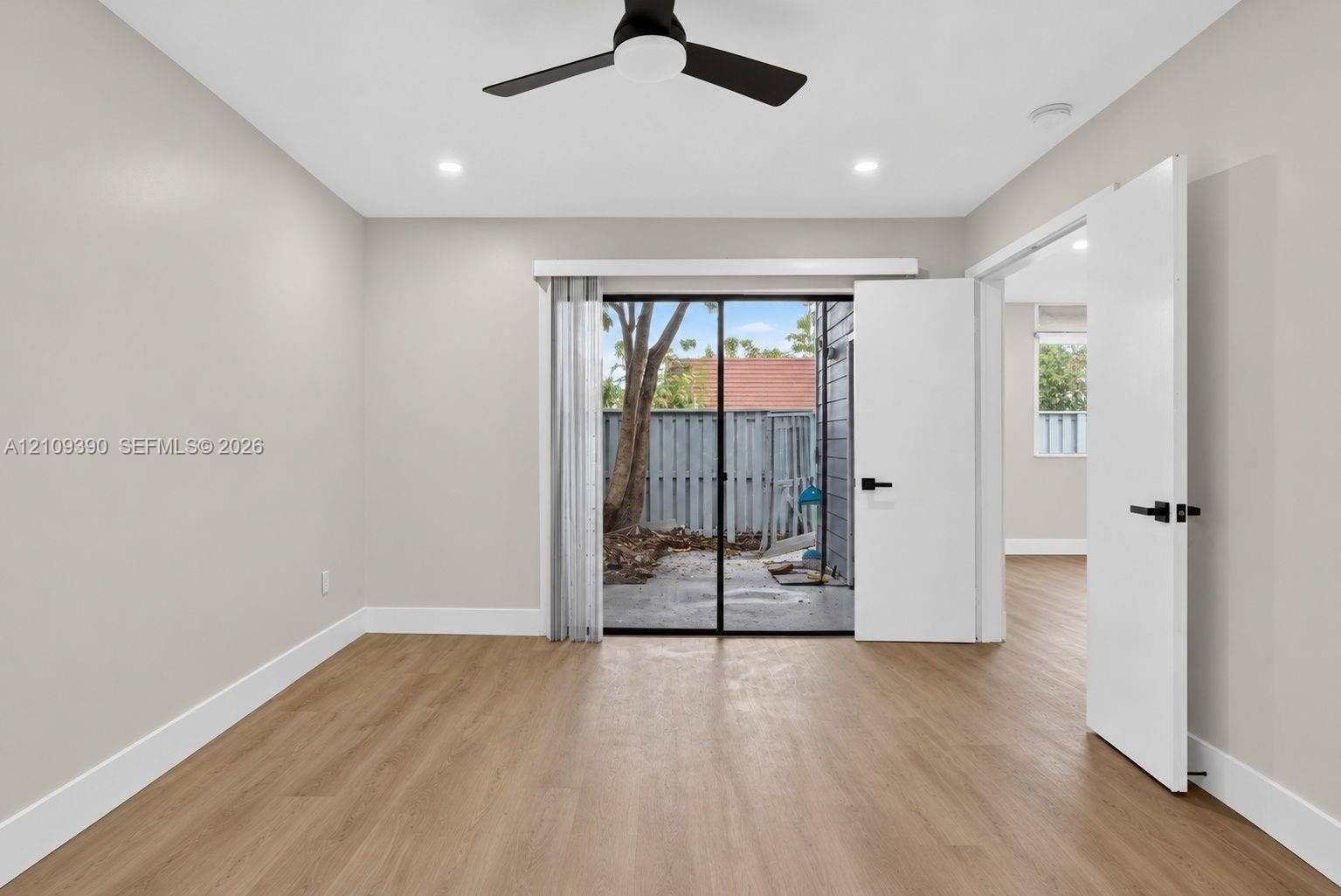 Neutral-toned room featuring wood-finish flooring, a matte black ceiling fan, recessed lighting, and a sliding glass door providing external access