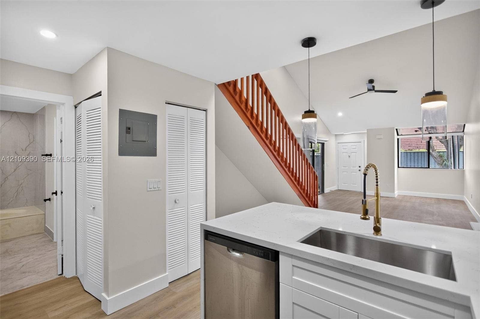 Kitchen featuring white cabinetry, stone-look countertop, undermount stainless steel sink, gold-tone faucet, and wood-finish flooring with an exposed staircase featuring a wooden handrail