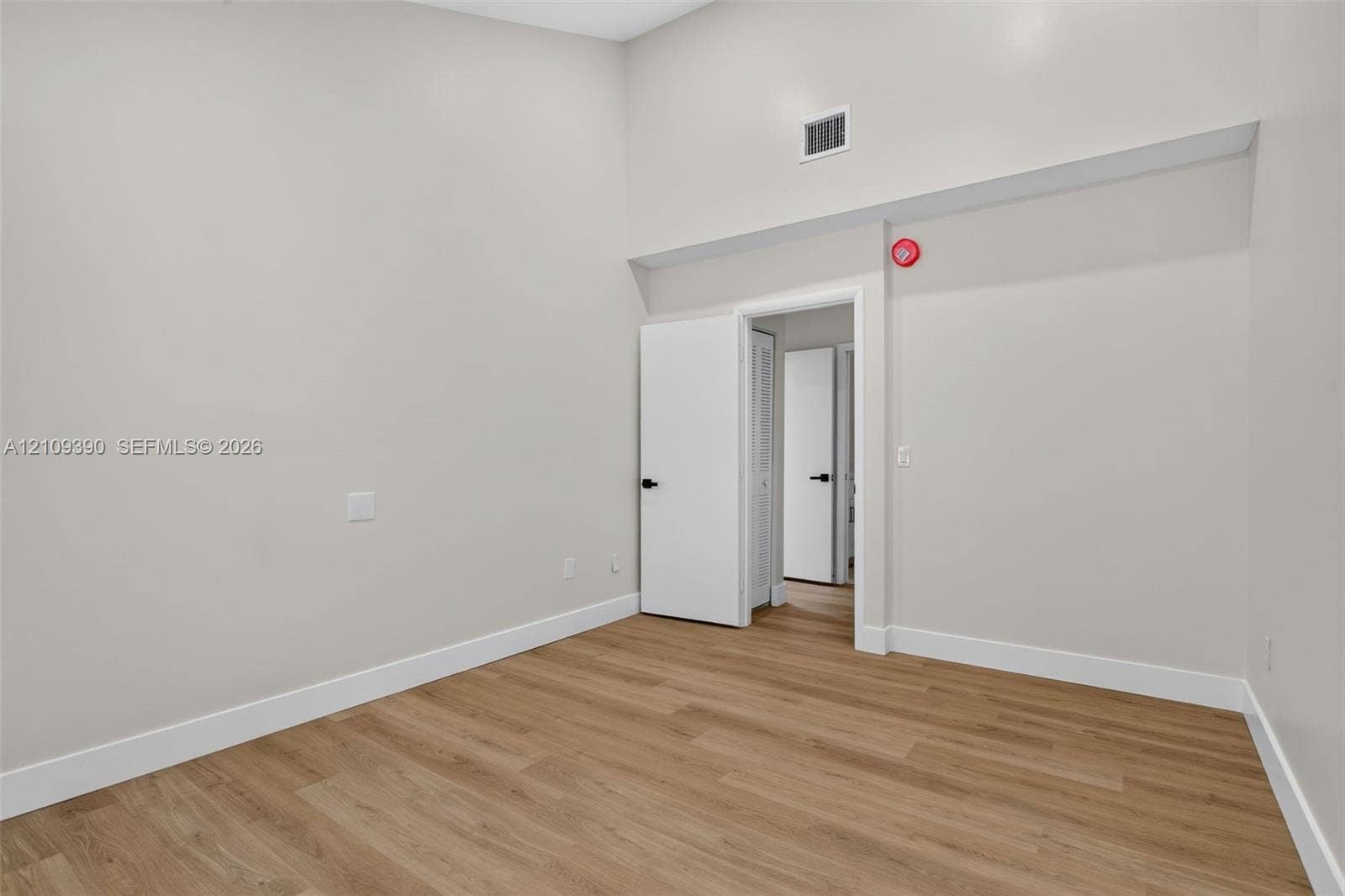 High-ceilinged room featuring wood-finish flooring and solid-core interior doors with matte black hardware