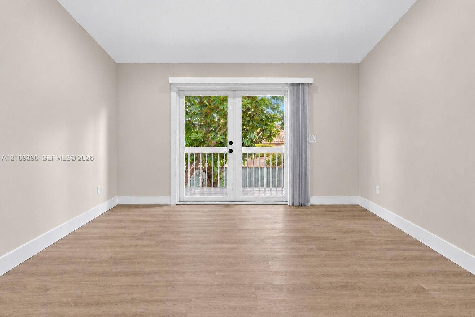 Neutral interior room featuring wood-finish flooring, white walls, and French doors opening to an exterior balcony