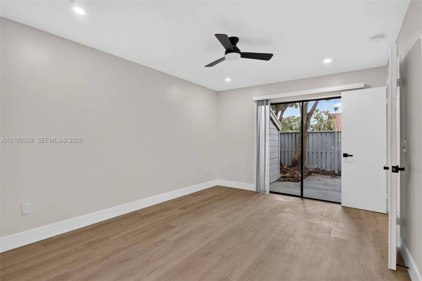 Neutral-toned interior featuring wood-finish flooring, recessed lighting, a matte black ceiling fan, and sliding glass doors with exterior access to a patio area