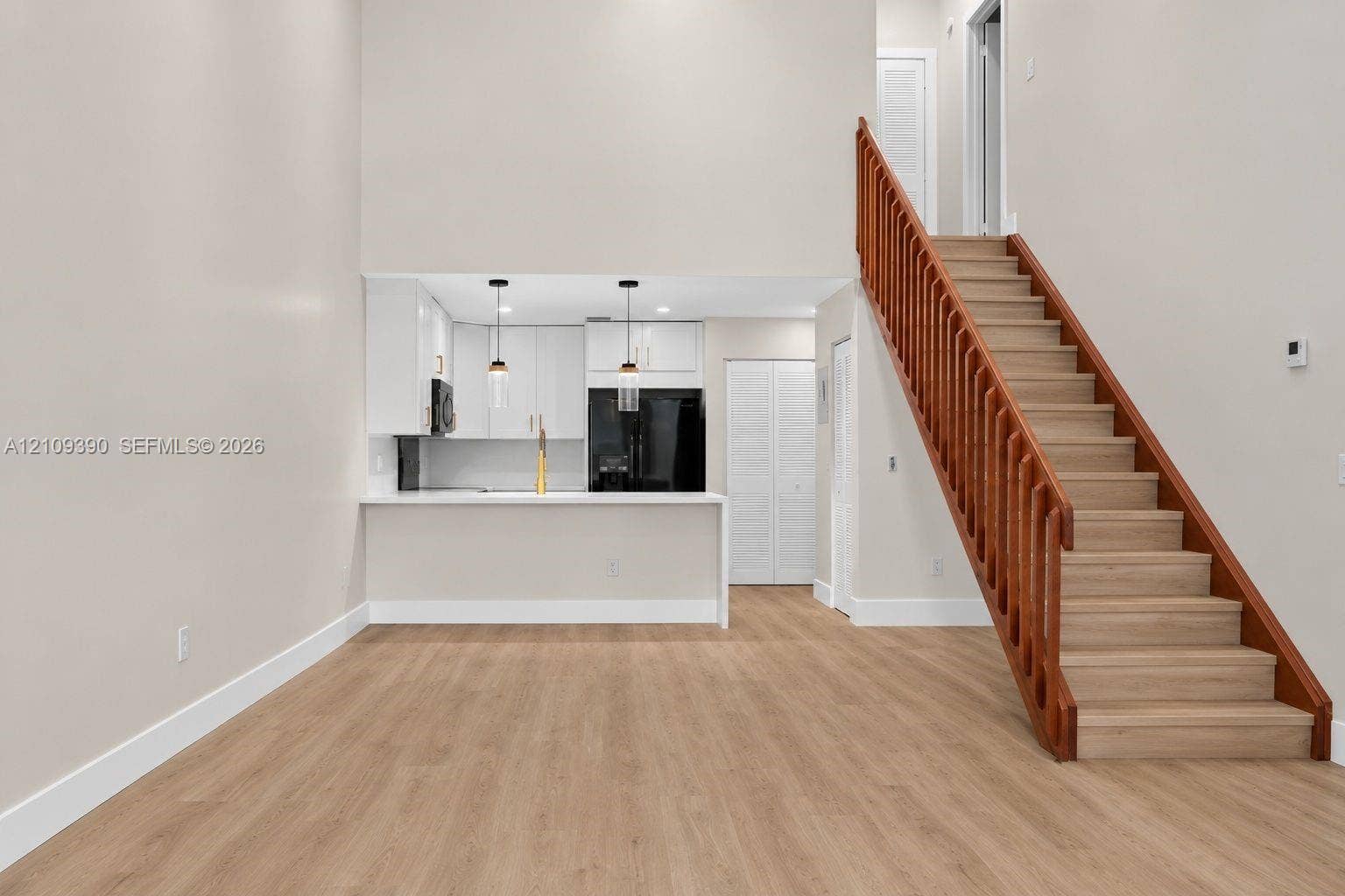 High ceilings, wood-finish flooring, staircase with a wood railing, kitchen with white cabinetry and a breakfast bar, and pendant lighting