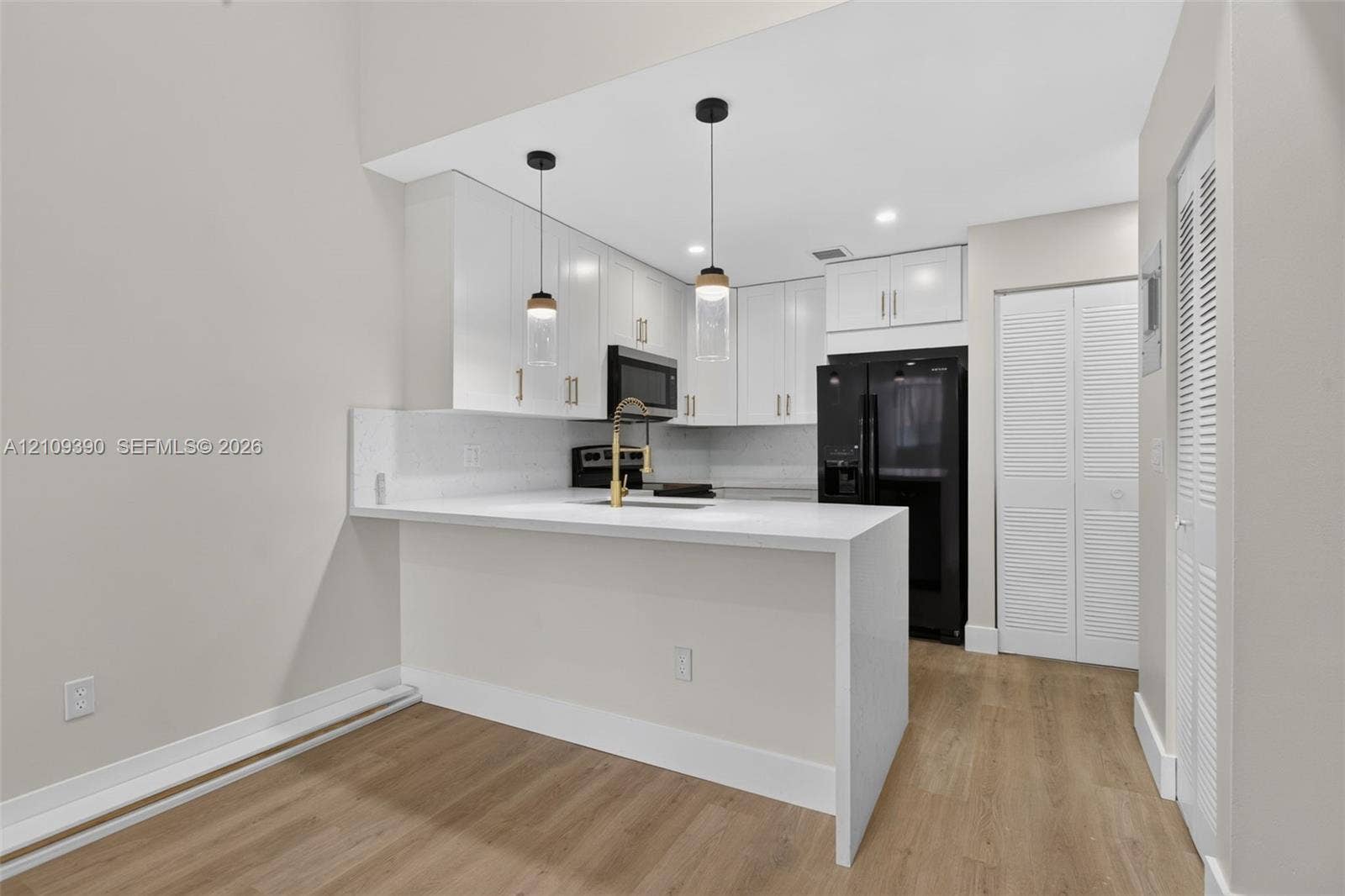 Kitchen featuring white shaker-style cabinetry, a quartz waterfall-edge peninsula, brass-finish faucet, pendant lighting, and wood-finish flooring
