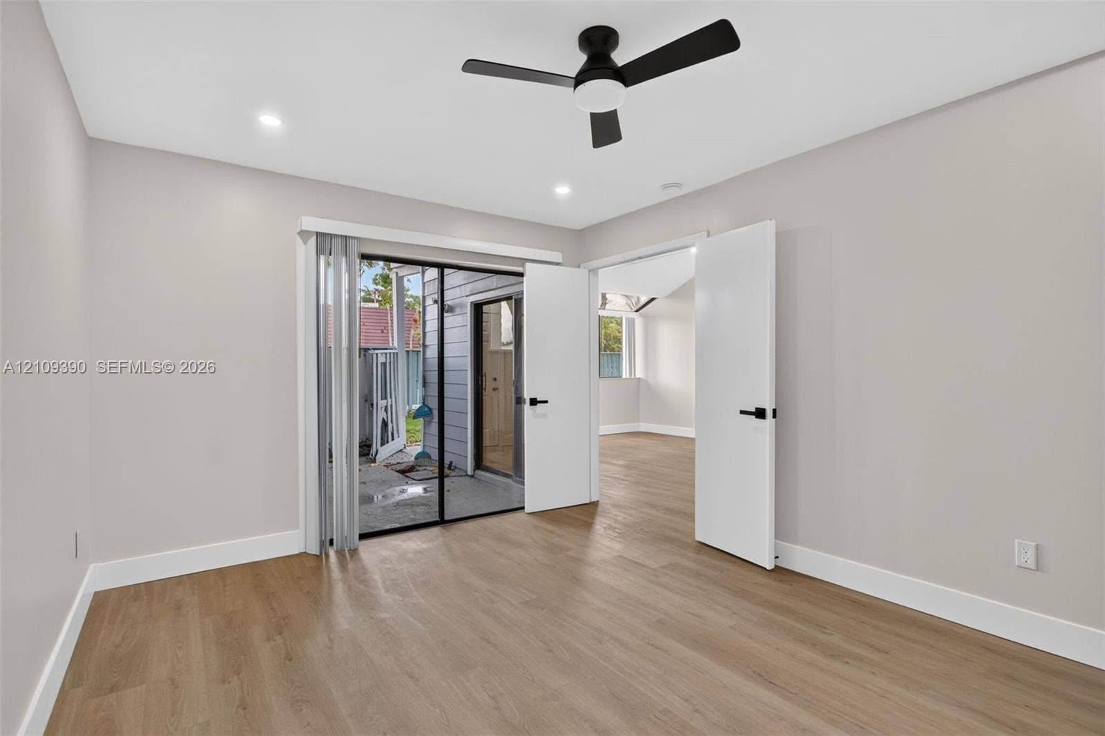 Room featuring wood-finish flooring, recessed lighting, a modern ceiling fan with integrated light, sliding glass doors, and dual-panel doors with matte black hardware