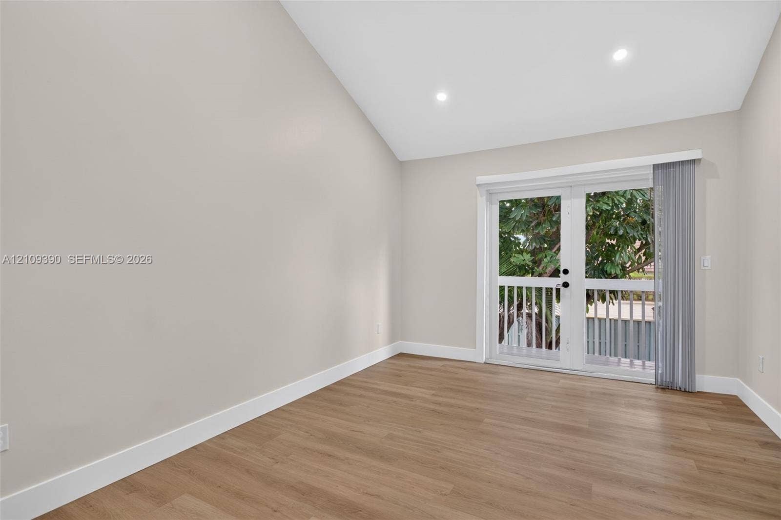 Vaulted ceilings, wood-finish flooring, recessed lighting, and double glass doors leading to an exterior balcony