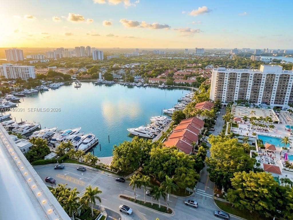 Aerial perspective of a coastal community featuring a deep-water marina, multiple high-rise structures, a private swimming pool, and established tropical landscaping