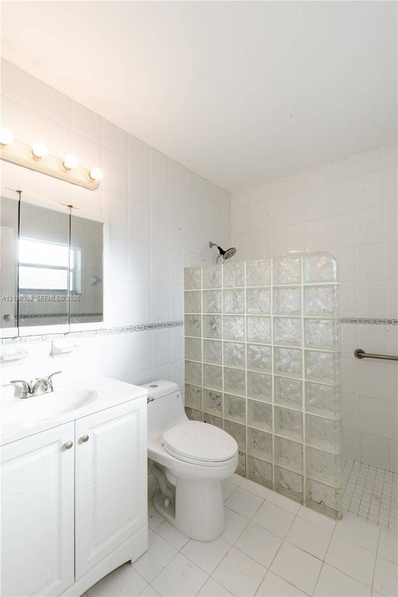 7641 Raleigh Street, #1, Hollywood, Hollywood, FL 33024 Bathroom featuring a white vanity cabinet, ceramic tile walls and flooring, a glass block shower wall, and a chrome-finish shower head