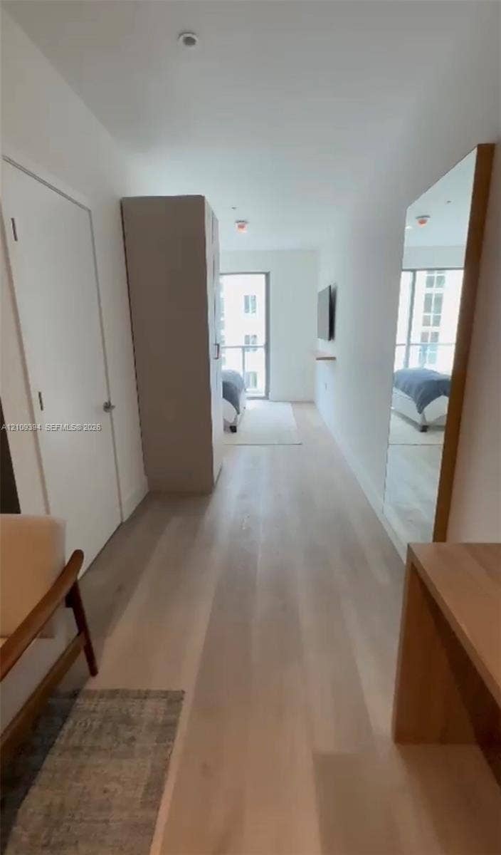 Interior space featuring light-toned wood-finish flooring, floor-to-ceiling mirror with wood frame, built-in storage cabinetry, and sliding glass door with access to an exterior balcony