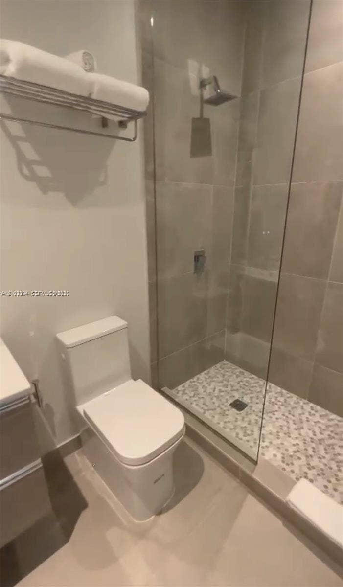 Glass-enclosed shower with pebble tile flooring, wall-mounted rainfall showerhead, and polished chrome fixtures