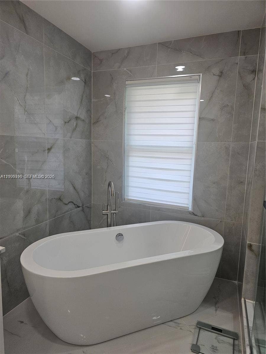 Freestanding soaking tub featuring a chrome floor-mounted faucet and large-format porcelain wall tile with a neutral-toned veined pattern