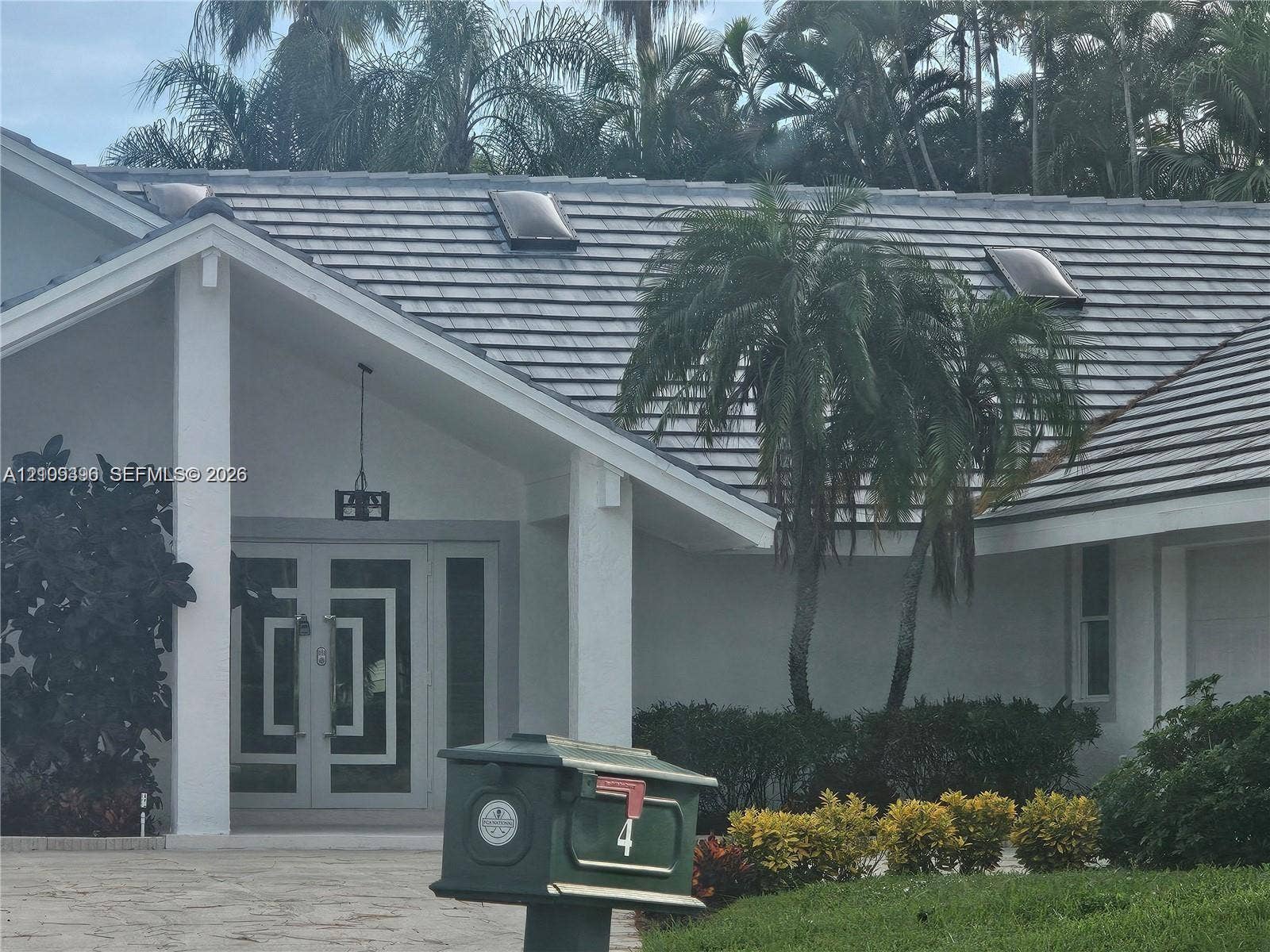 Exterior entrance featuring dual glass-panel doors with geometric detailing, gabled roofline, integrated skylights, and a covered portico with square structural columns