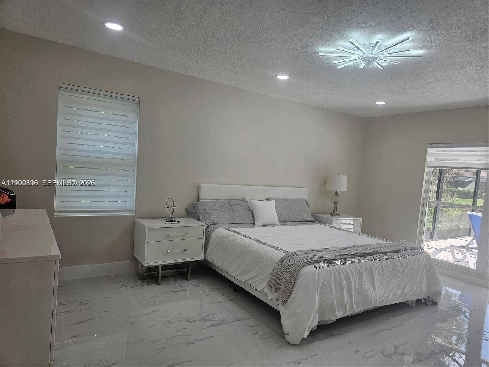 Polished stone-finish tile flooring, modern starburst ceiling fixture, recessed lighting, and dual windows with integrated shades