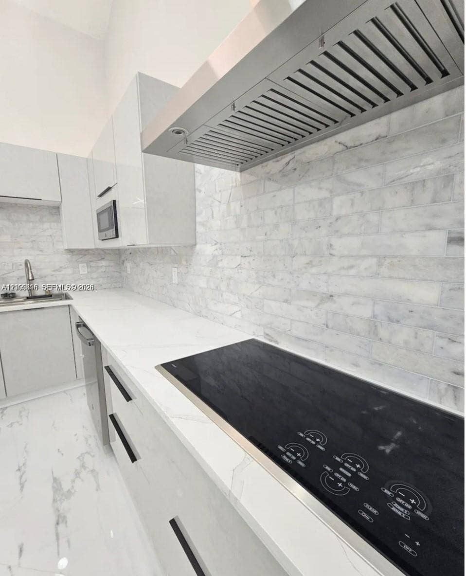 Contemporary kitchen featuring high-gloss cabinetry, stone-finish countertops, subway tile backsplash, a stainless steel range hood, and integrated electric cooktop
