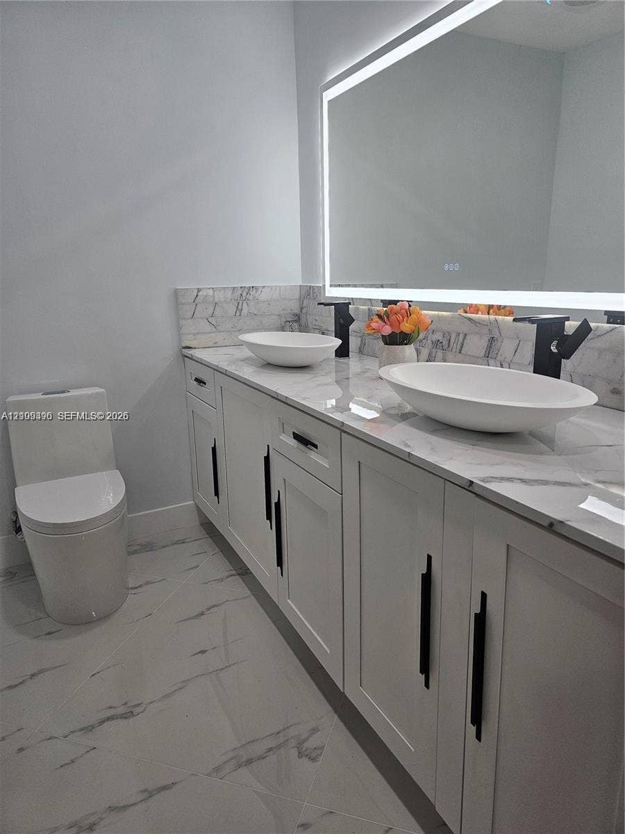 Double vanity with stone-finish countertop, dual vessel sinks, matte black fixtures, LED-integrated mirror, and large-format porcelain tile flooring