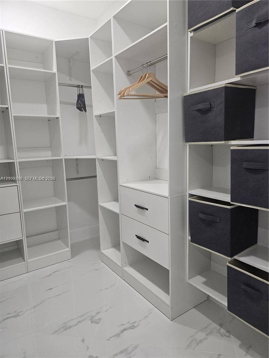 Custom reach-in closet featuring white floor-to-ceiling built-in shelving, integrated hanging rods, two soft-close drawers with matte black hardware, and polished stone-finish flooring