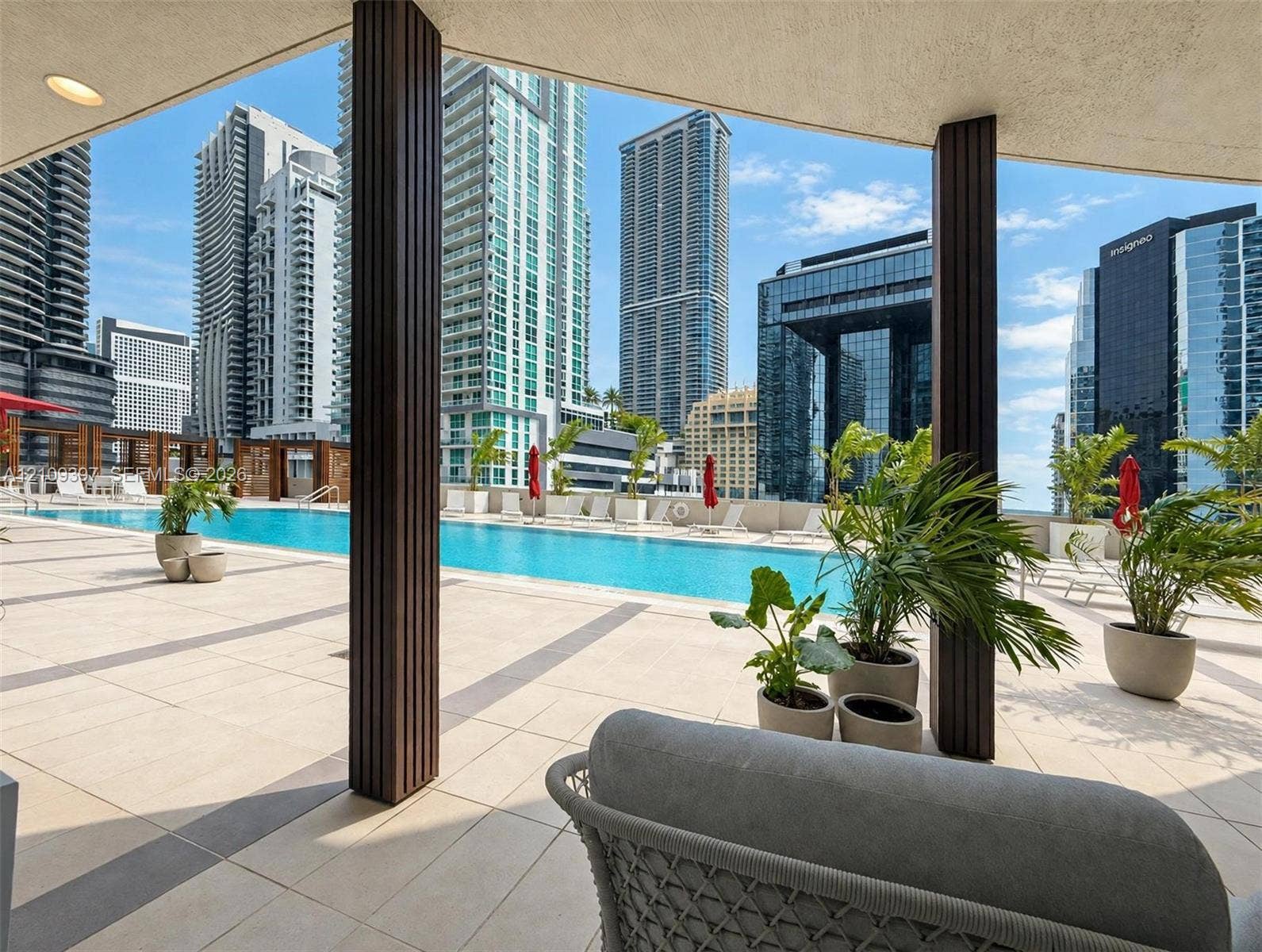 Covered terrace featuring large-format tile flooring and structural columns, overlooking a linear swimming pool with a hardscaped deck