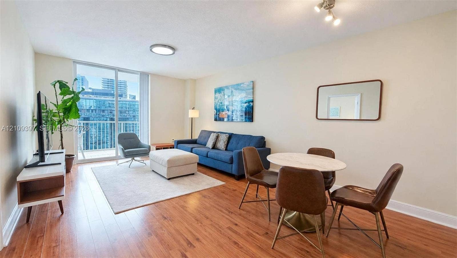 Open-concept interior featuring wood-finish flooring, ceiling-mounted lighting, and a large sliding glass door providing access to a private balcony