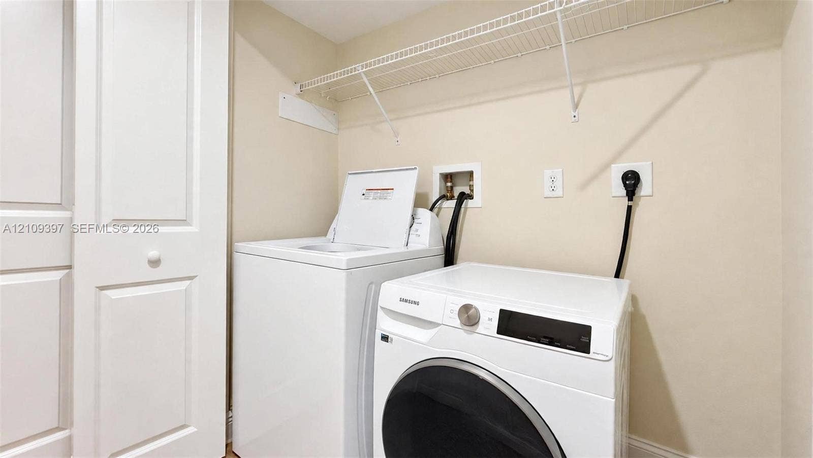 Laundry area featuring built-in shelving, white paneled door, and recessed utility hookups