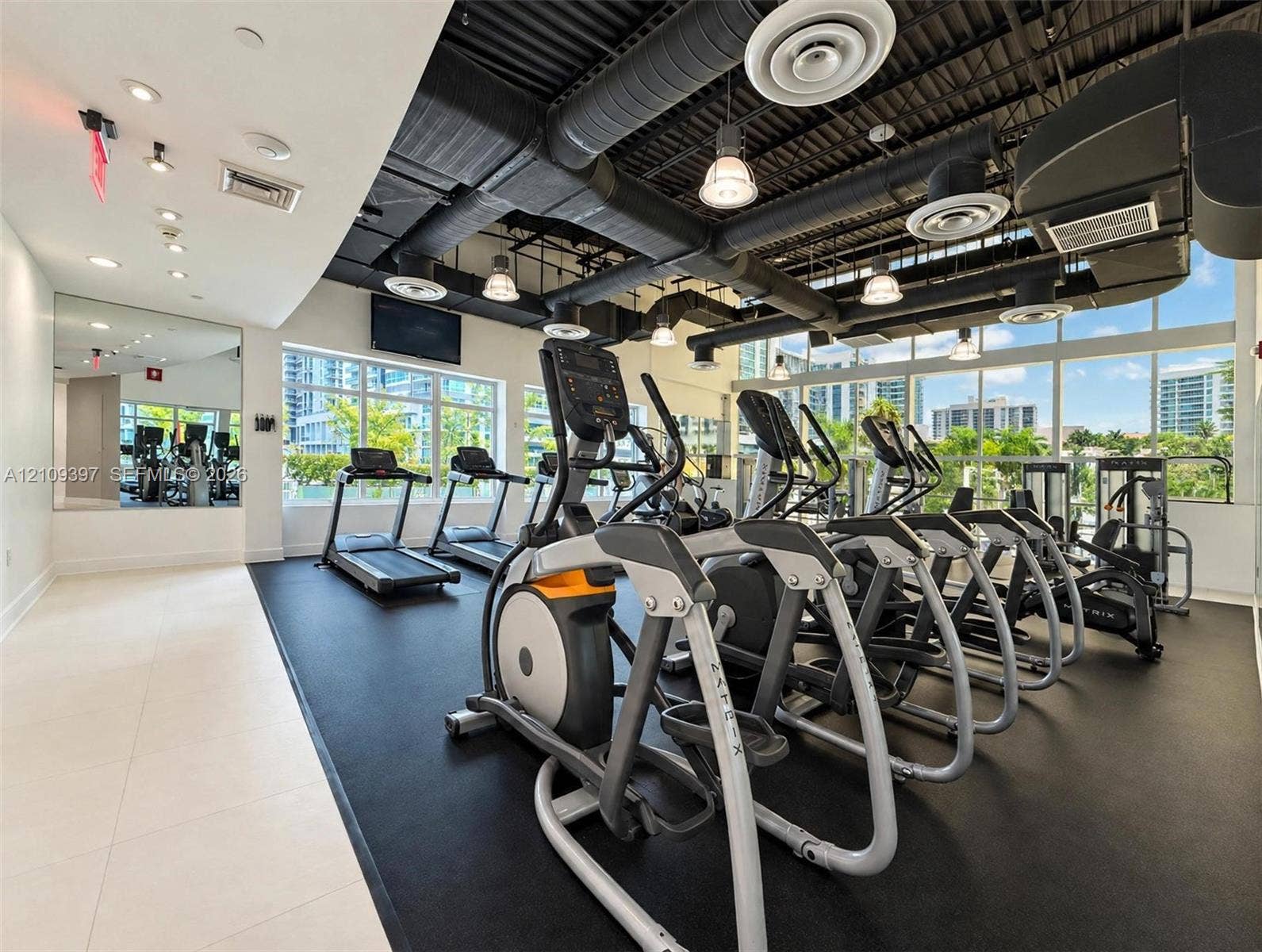 Fitness center featuring an exposed industrial ceiling, floor-to-ceiling windows, rubberized flooring, and wall-to-wall mirrors