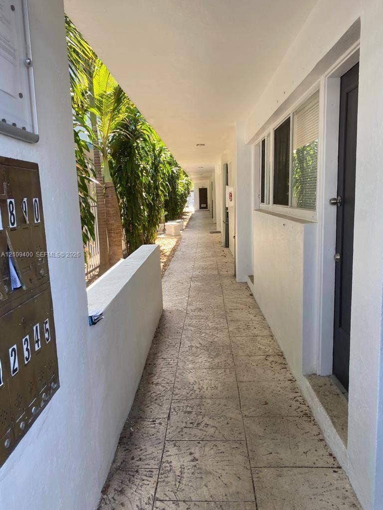 Exterior walkway featuring stone-tile flooring, metal wall-mounted mailboxes, and white stucco walls