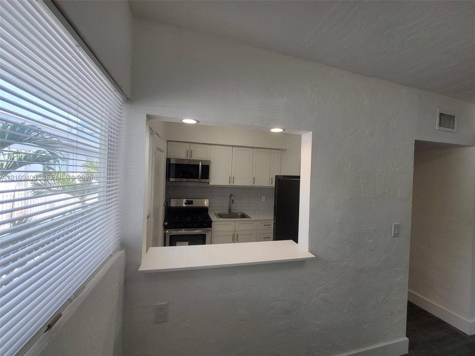 Kitchen pass-through window with a white countertop, recessed lighting, white shaker-style cabinetry, stainless steel appliances, and tile backsplash