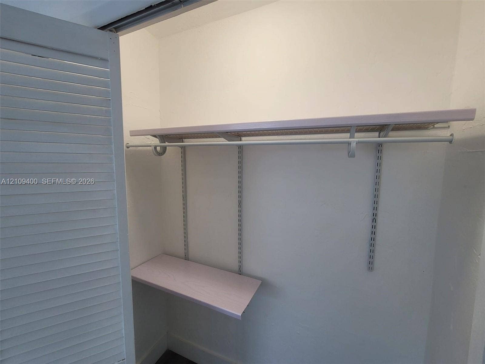 Storage closet featuring louvered bi-fold doors, adjustable metal shelving standards, and integrated hanging rods