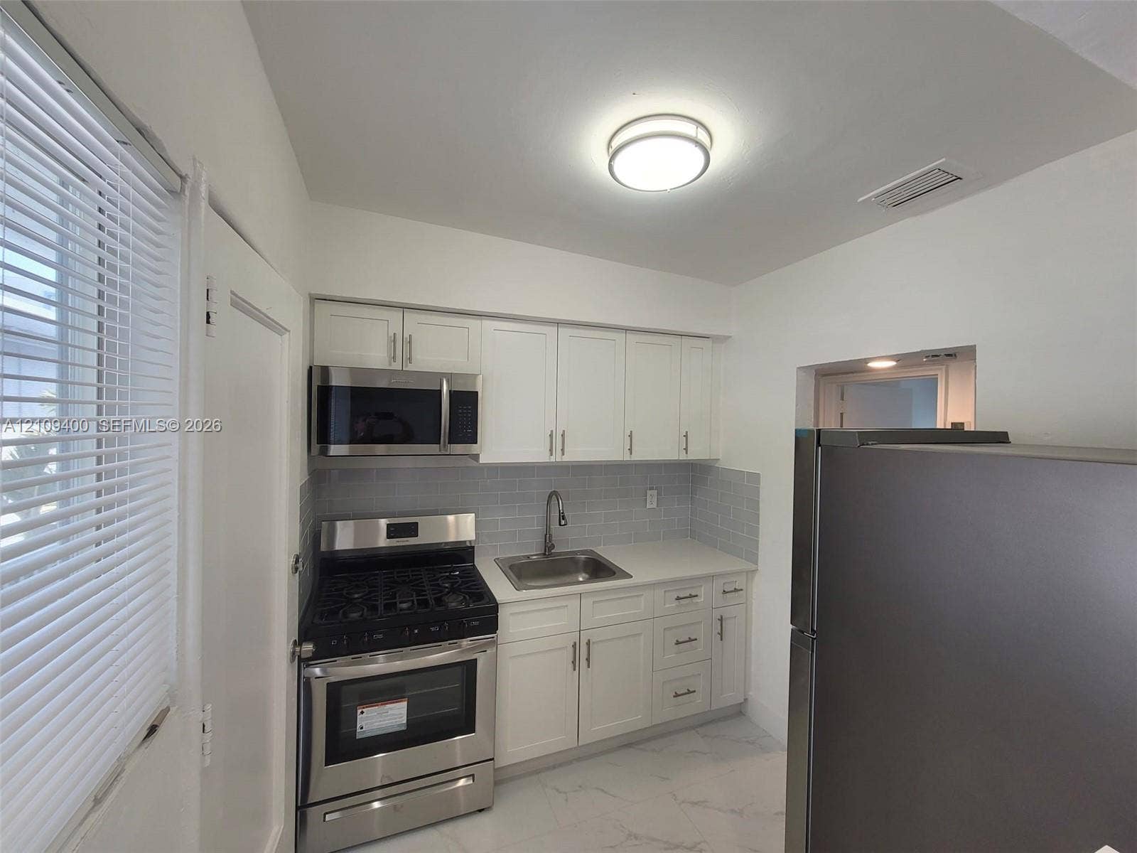 Kitchen featuring white shaker-style cabinetry, stainless steel appliances, a light-toned stone-finish countertop, a subway tile backsplash, and polished tile flooring