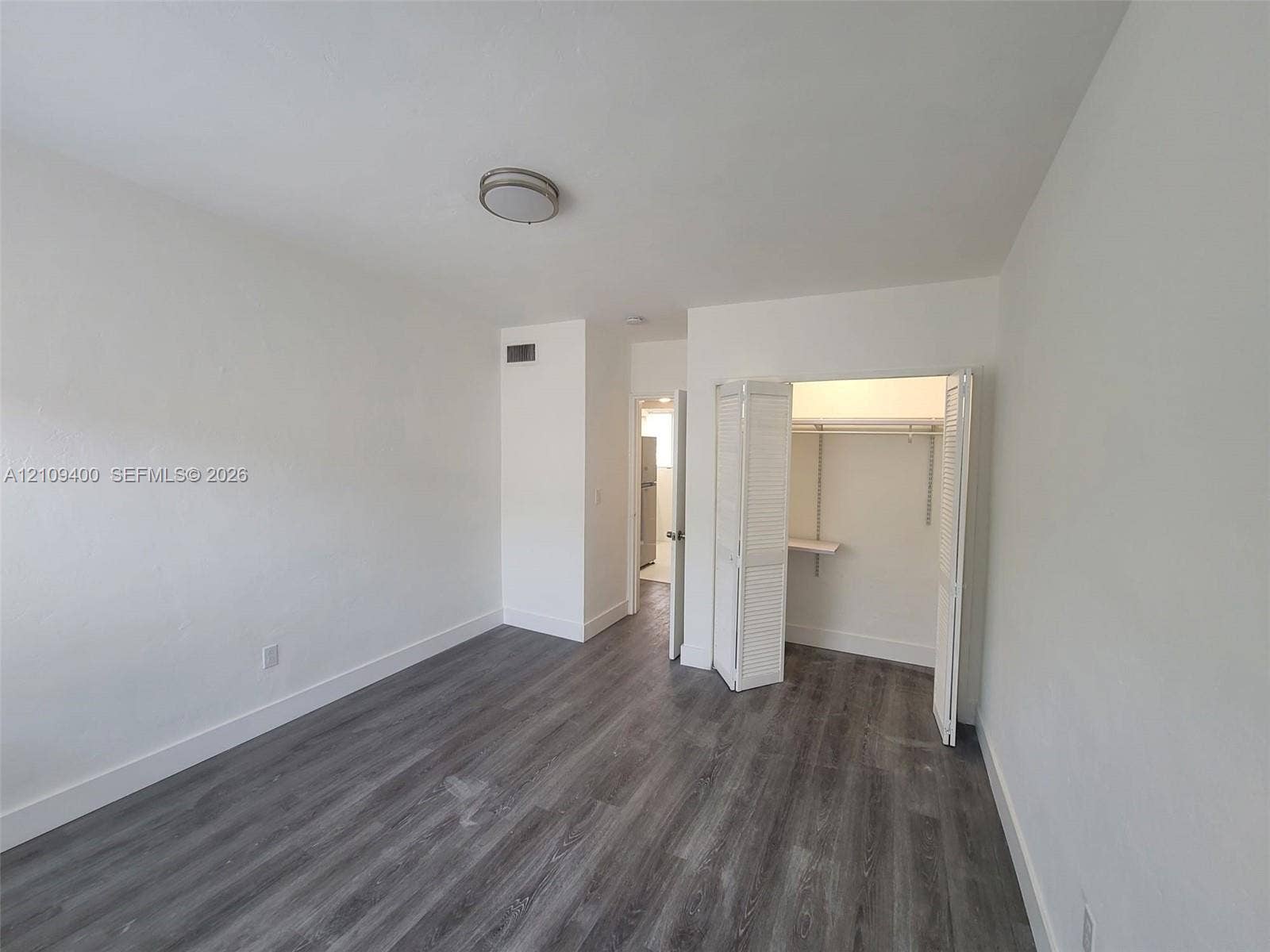 Room featuring wood-finish flooring, white walls, flush-mount ceiling lighting, and a closet with bifold louvered doors