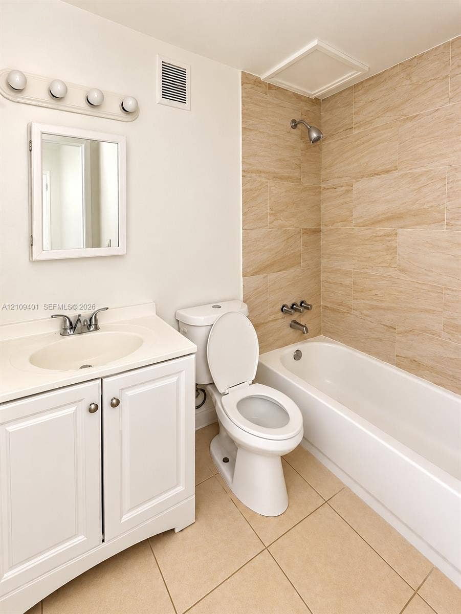 White vanity cabinet with integrated basin, polished metal faucet, recessed medicine cabinet, tiled tub surround, and ceramic floor tiling