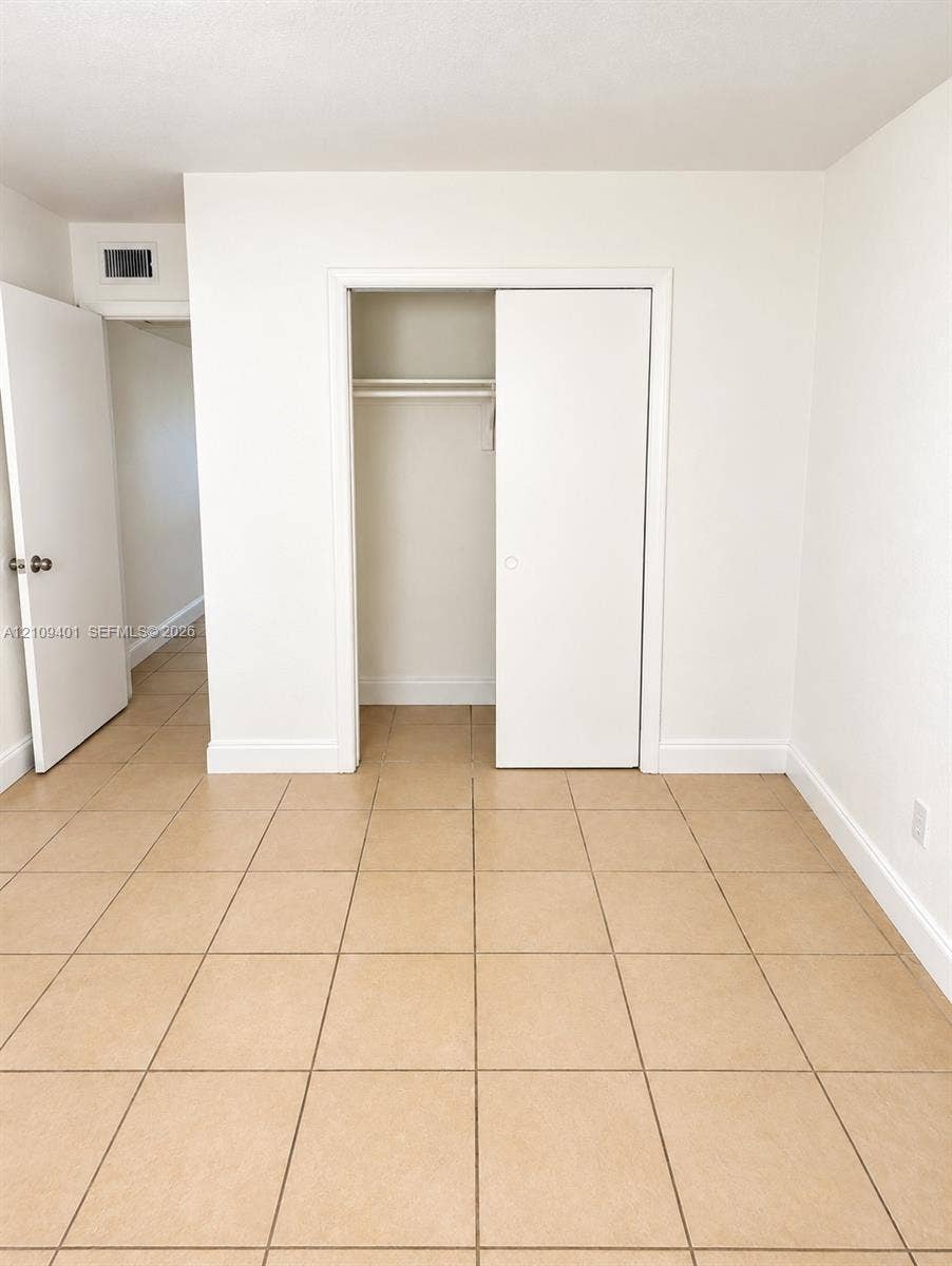 Neutral-toned tile flooring, white interior doors, and a closet featuring a built-in hanging rod