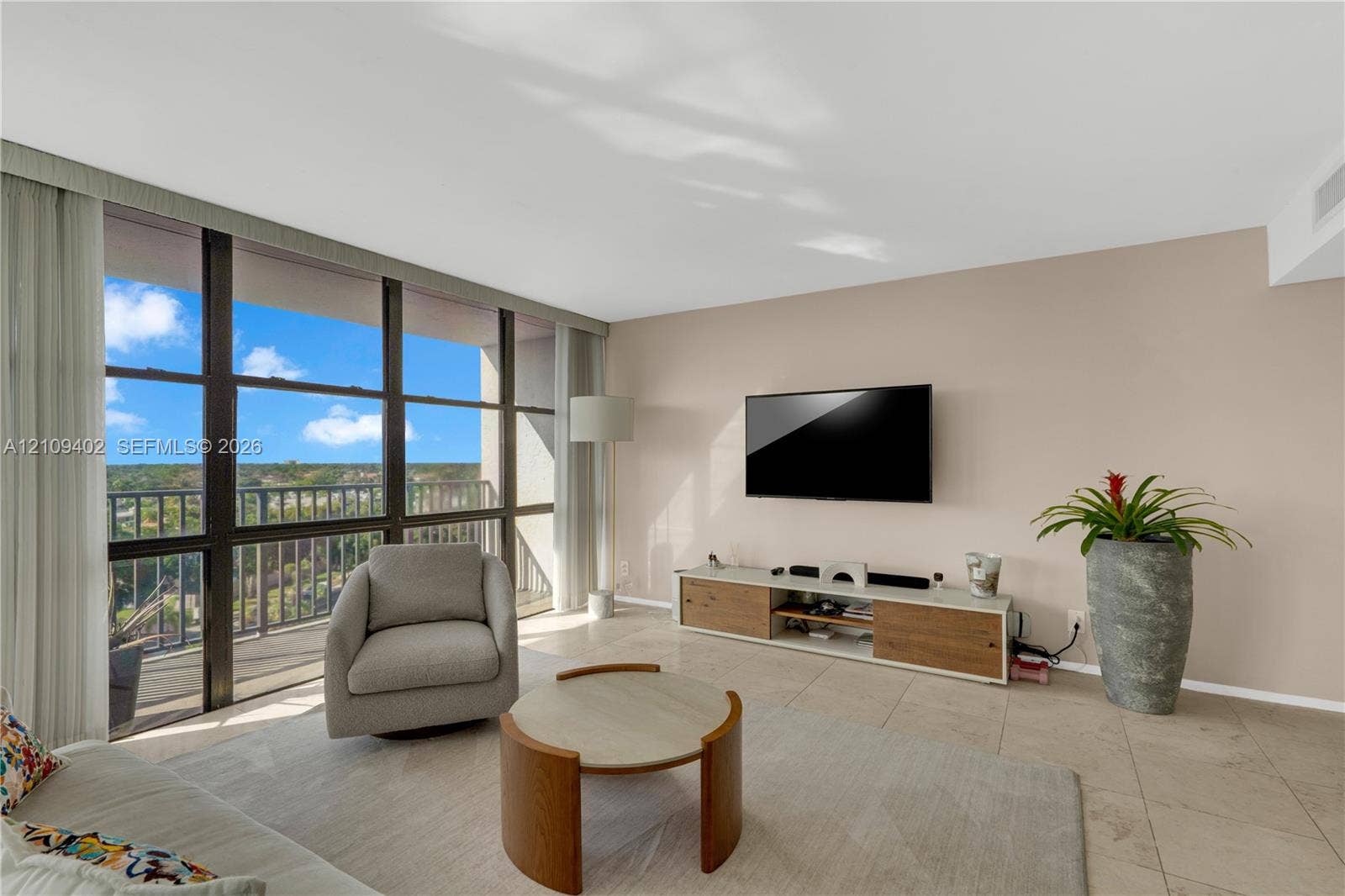 Living area featuring floor-to-ceiling windows, natural stone tile flooring, and a private balcony with metal railing