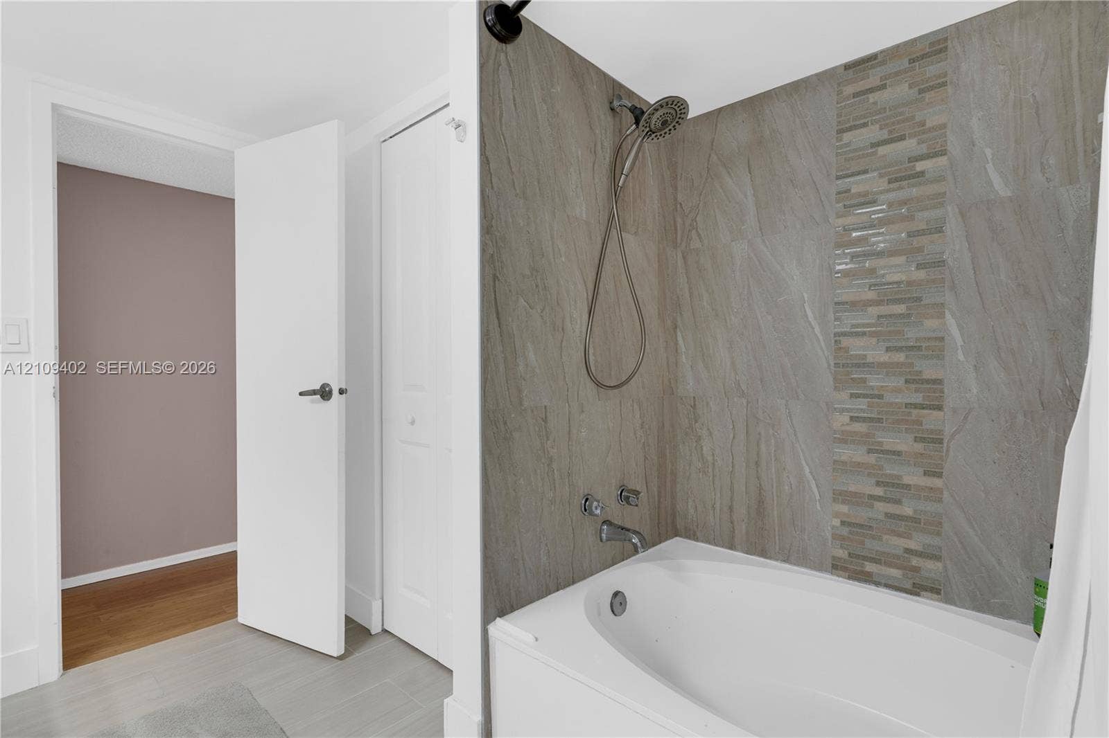 Bathtub featuring a tiled surround with stone-finish panels, vertical mosaic accent inlay, handheld showerhead, and wall-mounted faucet