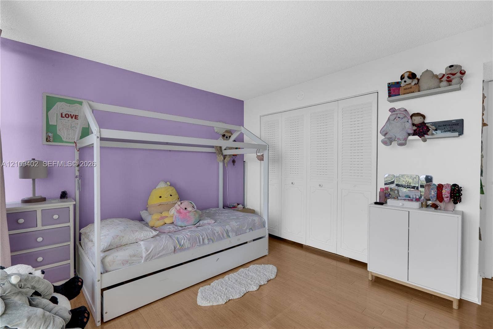 Room featuring wood-finish flooring, white louvered-style closet doors, and an accent wall