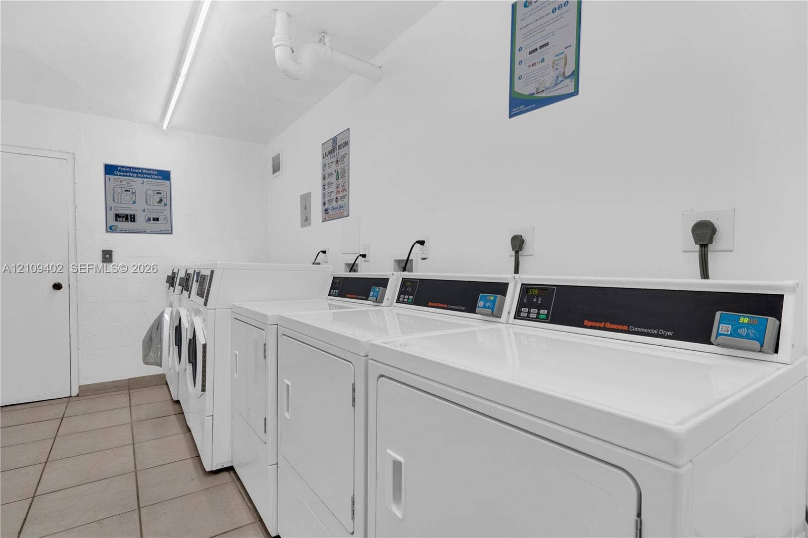 Laundry facility featuring multiple high-capacity commercial-grade dryers, tiled flooring, and industrial-style linear lighting